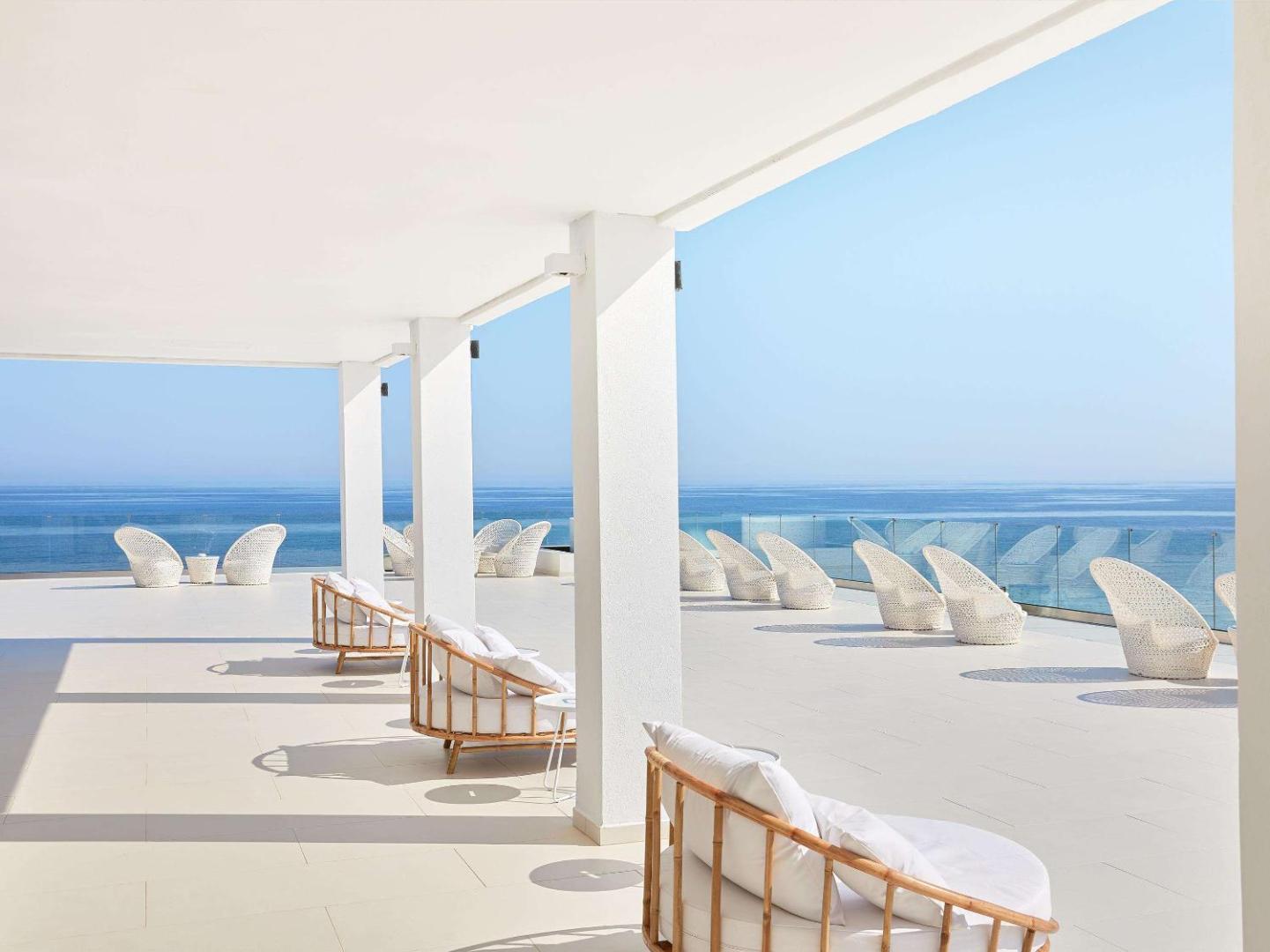 Grecotel Lux Me White Palace viesnīcas atpūtas terase ar baltiem pītiem krēsliem un skatu uz Vidusjūru Krētā