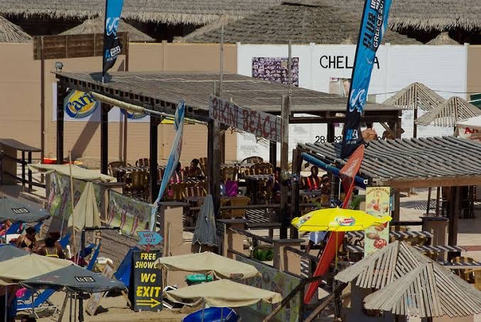 Bikini Beach bārs pie Enorme Ammos Beach Resort viesnīcas — mājīga āra terase ar galdiņiem un krāsainiem saulessargiem