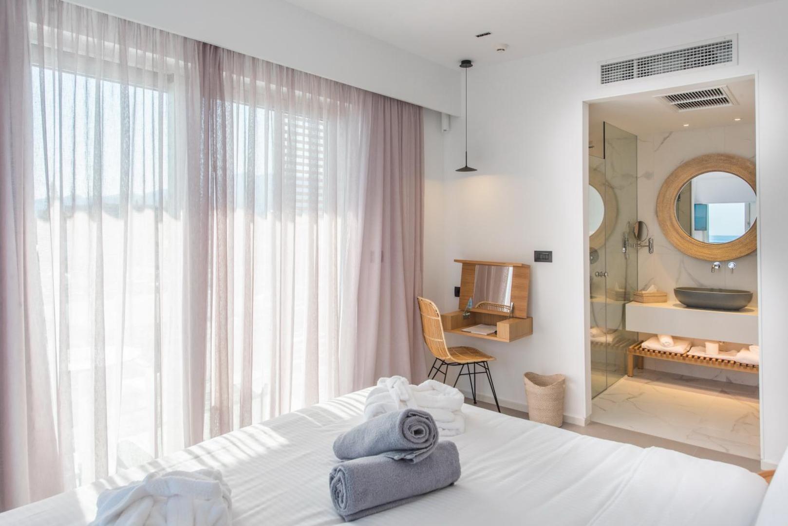 Enorme Ammos Beach Resort numurs ar atvērtā plānojuma vannasistabu, apaļu spoguli un gaišu dizainu