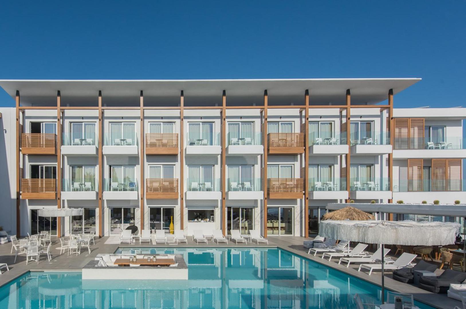 Enorme Ammos Beach Resort galvenā ēka un āra baseins dienas laikā Malijā — balti atpūtas krēsli un saulessargi pie ūdens