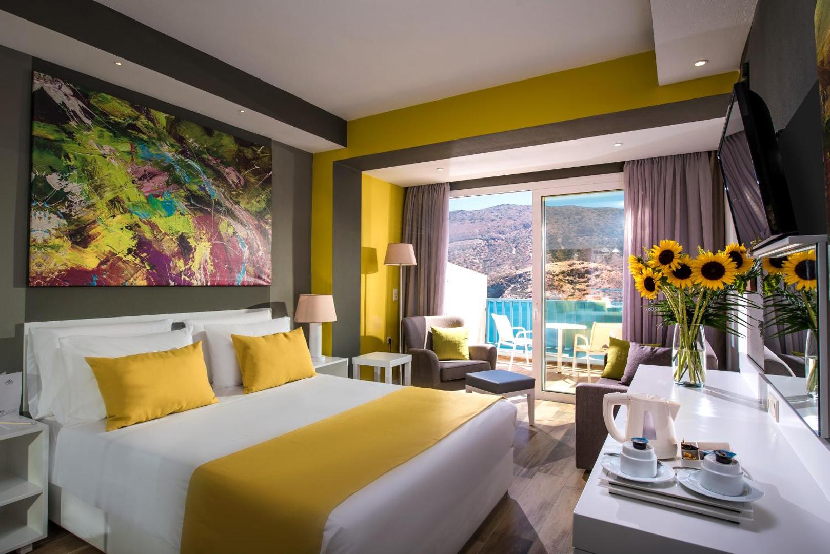 Moderns Fodele Beach & Water Park Resort numurs ar dzelteniem akcentiem, lielu gultu un skatu uz kalniem no balkona