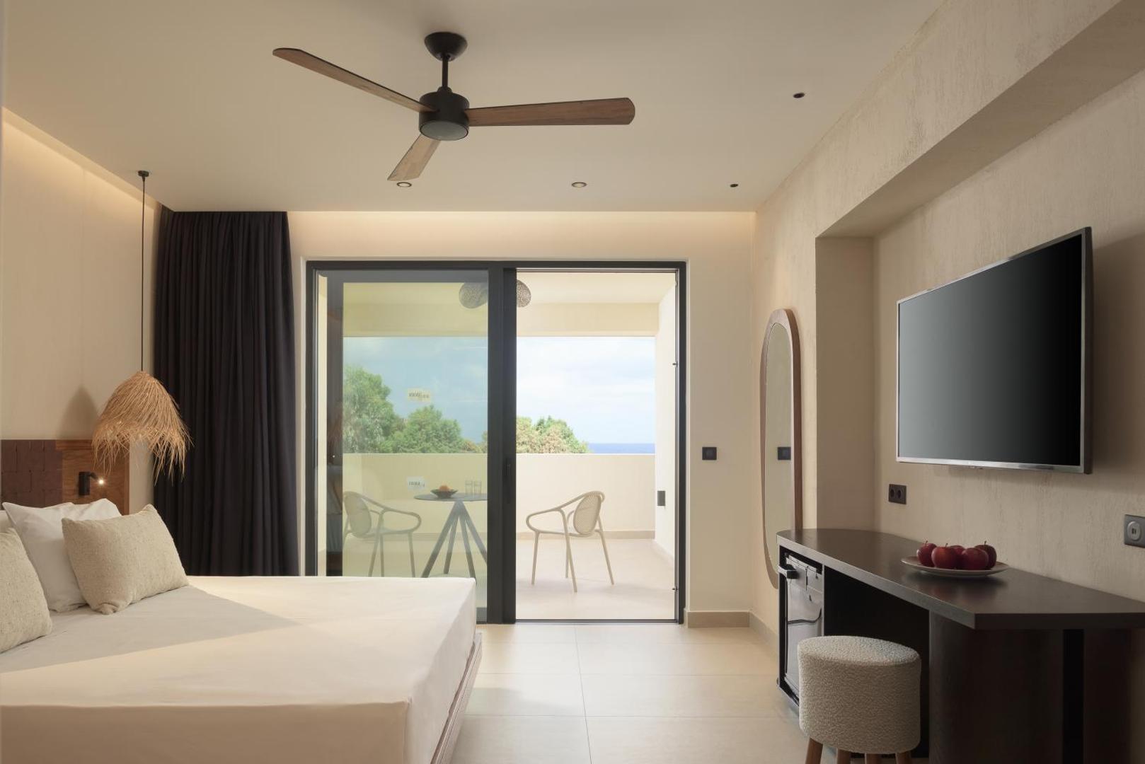 Fodele Beach & Water Park Resort moderns numurs ar balkonu, griestu ventilatoru, TV un darba zonu siltos toņos