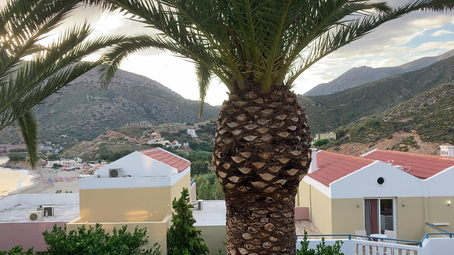 Skats no Fodele Beach & Water Park Resort teritorijas uz bungalo tipa numuriem ar sarkaniem dakstiņu jumtiem un palmu