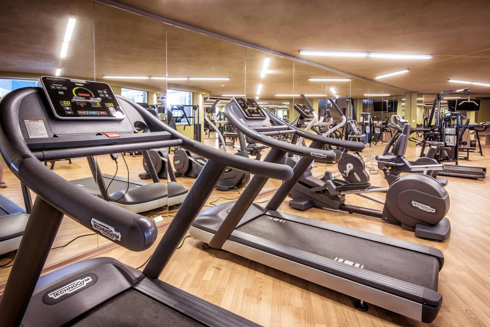Fodele Beach & Water Park Resort trenažieru zāle ar Technogym skrejceļiem un eliptiskajiem trenažieriem, plašiem spoguļiem un koka grīdu