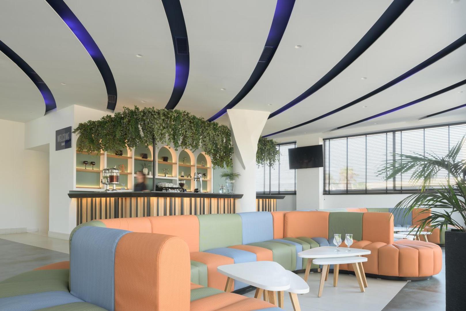 Lyttos Beach modernais lobby bārs ar krāsainiem dīvāniem, stilīgu griestu apgaismojumu un zaļumiem rotātu leti.