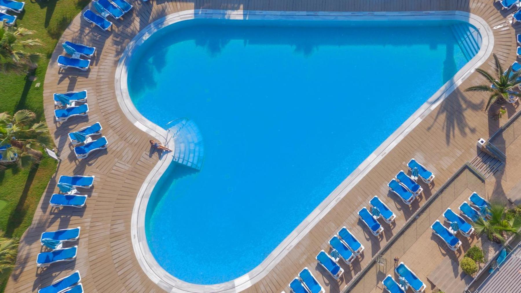 Lyttos Beach sirds formas āra baseins ar ziliem sauļošanās krēsliem un koka klāju skatā no putna lidojuma