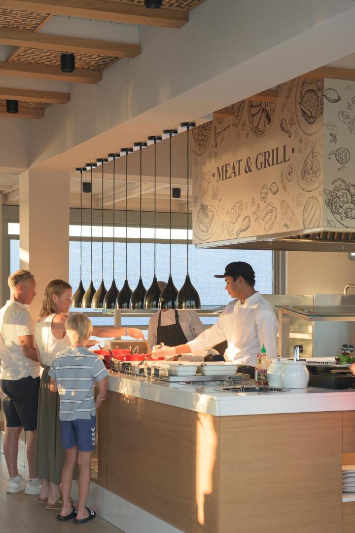 Viesnīcas Lyttos Beach restorāna bufetes zona Meat & Grill, kur pavārs apkalpo ģimeni ar bērnu