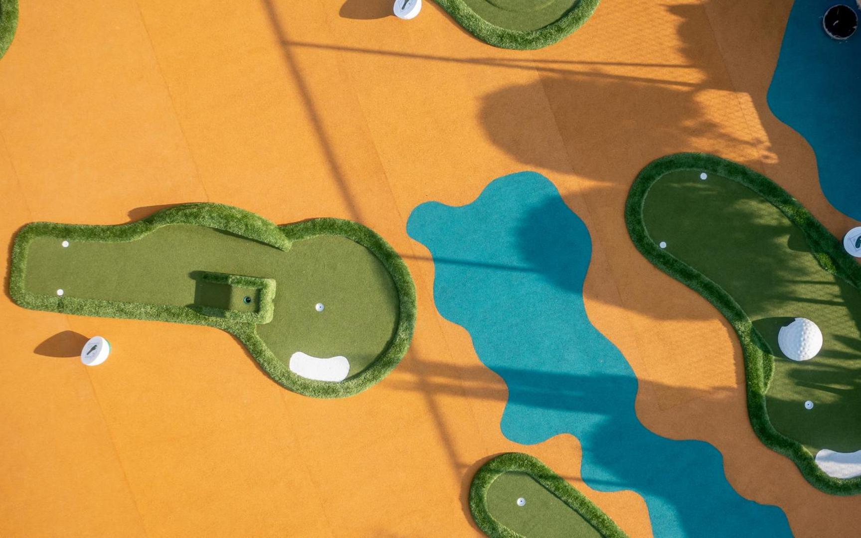 Lyttos Beach minigolfa laukums no augšas — krāsains segums ar zaļiem zāliena laukumiem un ūdens imitācijas elementiem