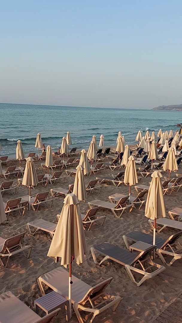 Cactus Beach viesnīcas privātā smilšu pludmale Stalidā, Krētā ar daudziem saulessargiem un sauļošanās krēsliem pie dzidri zilās jūras