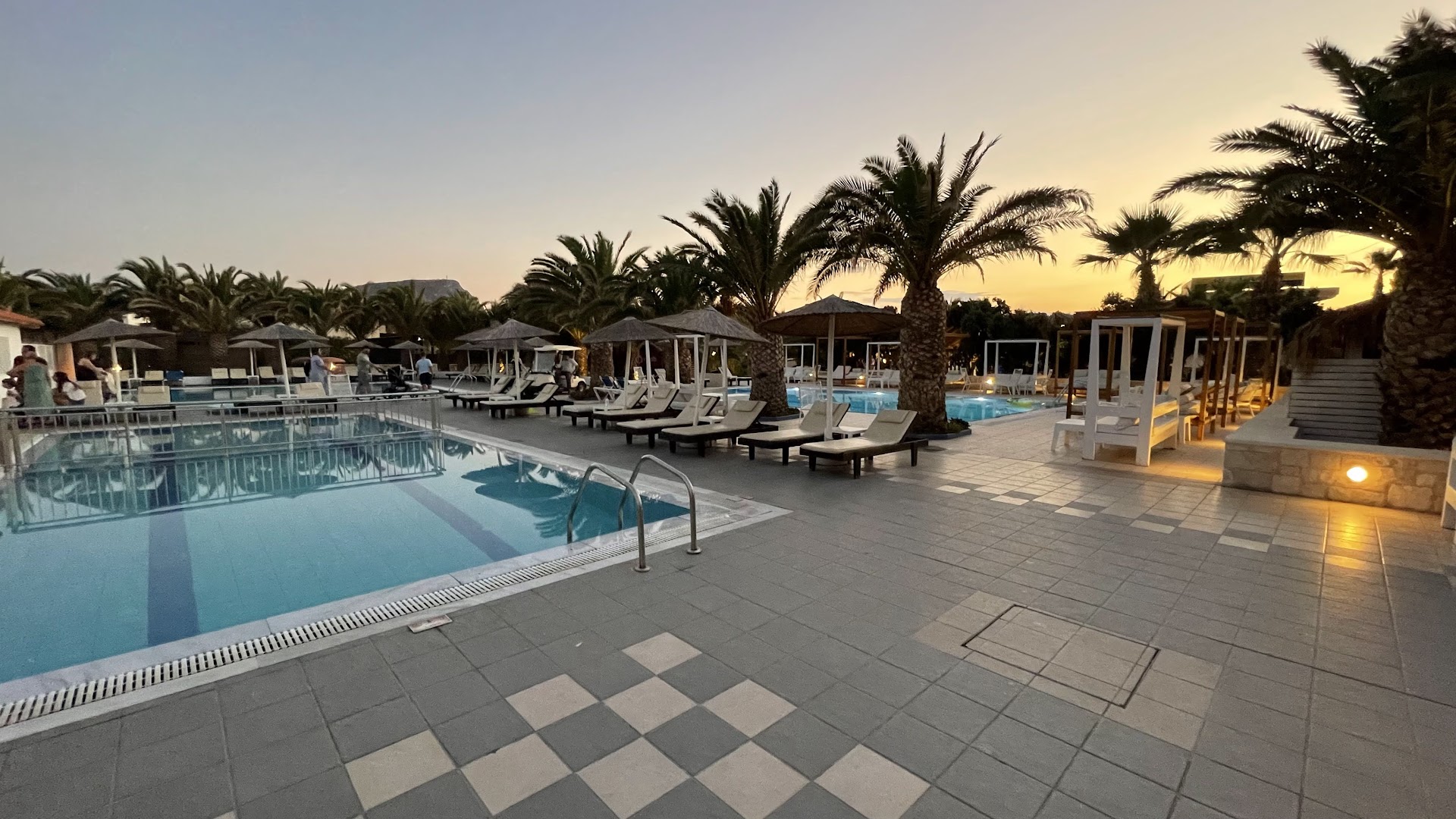 Stella Village Seaside Hotel āra baseins saulrietā — sauļošanās krēsli, saulessargi un palmas piekrastes viesnīcas teritorijā Analipsi