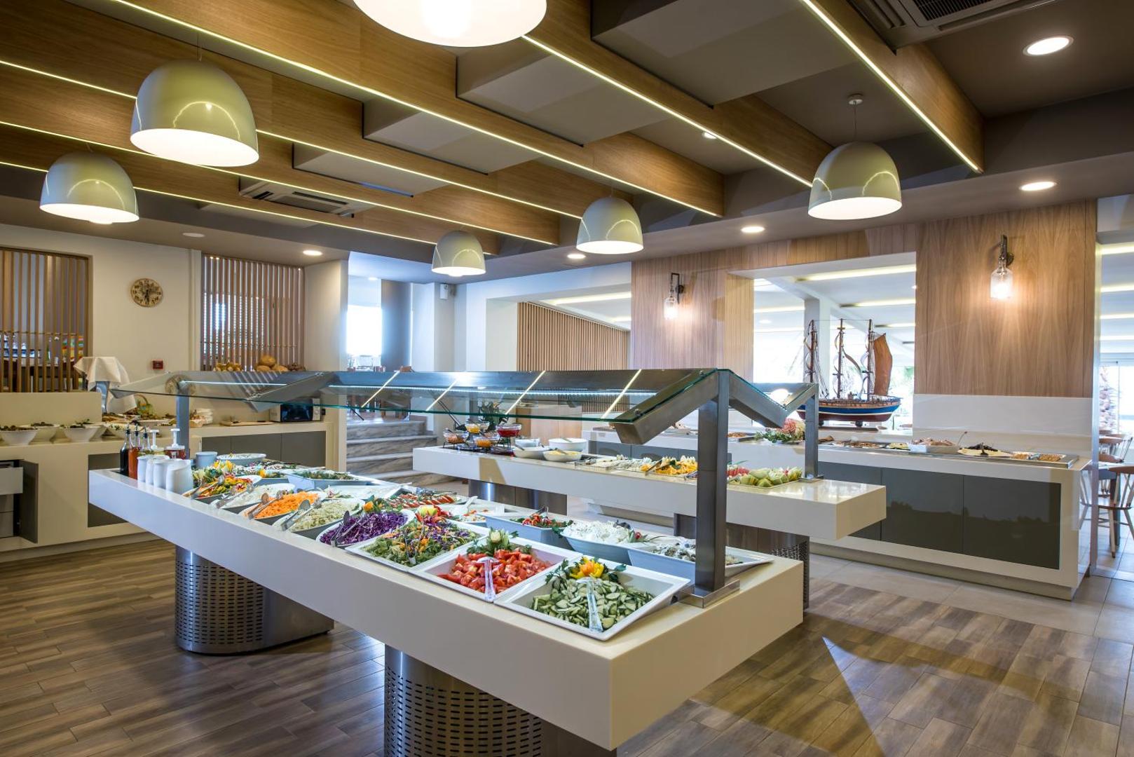 Stella Village Seaside Hotel galvenais restorāns ar bagātīgu bufetes galdu, svaigiem salātiem un dārzeņiem modernā, gaišā interjerā Hersonisā, Krētā.