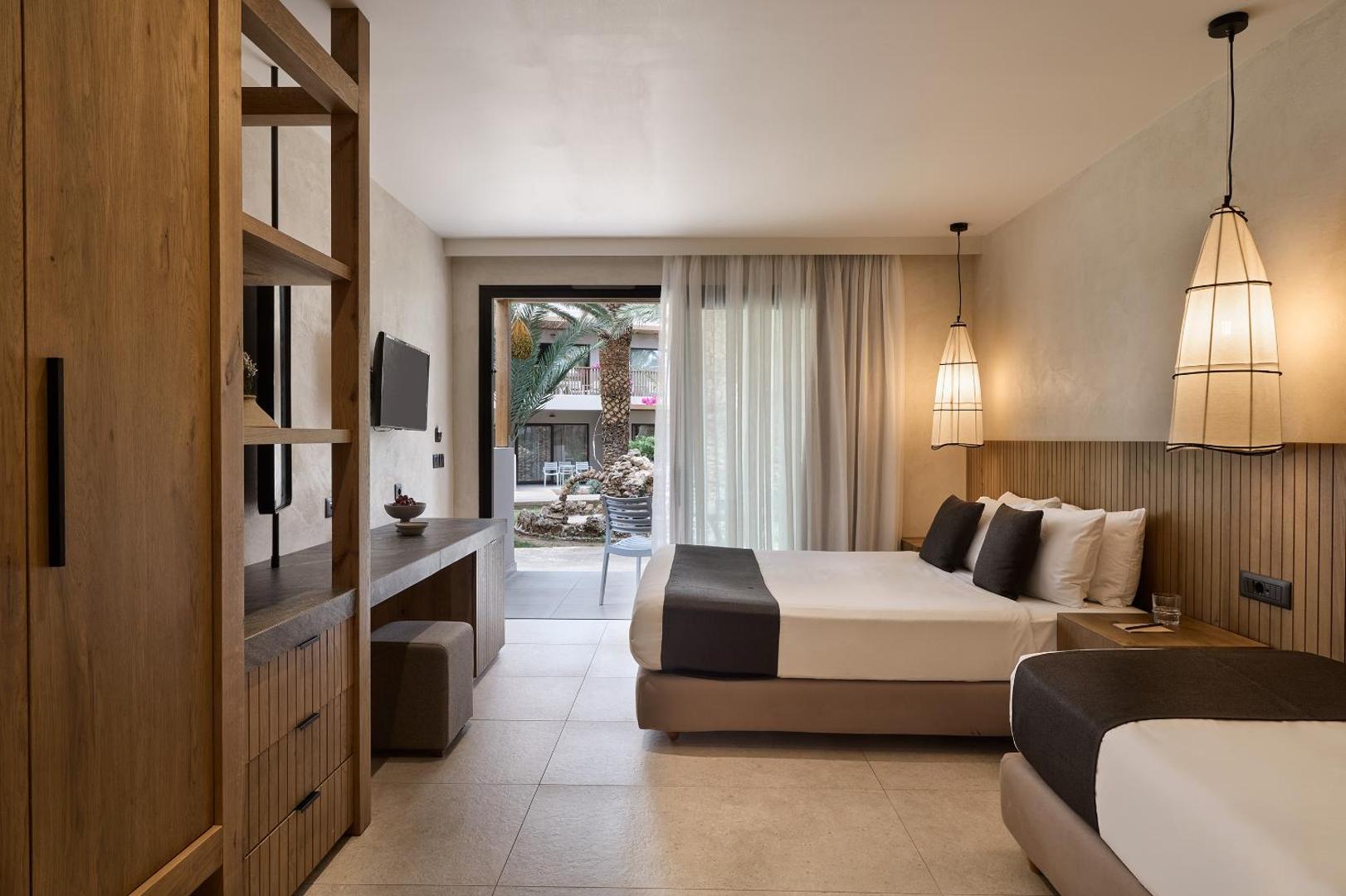 Stella Village Seaside Hotel ģimenes numurs ar divām gultām, koka mēbelēm un izeju uz terasi pie dārza Krētas kūrortā
