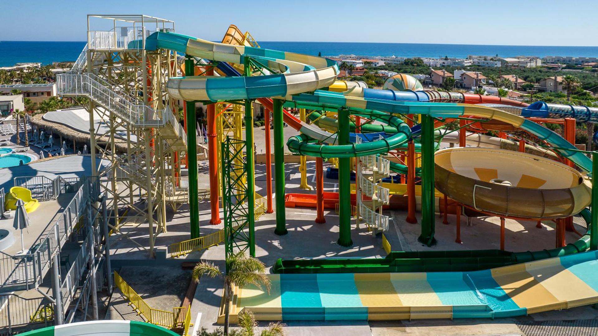 Stella Village Seaside Hotel augstie ūdens slidkalniņi ar skatu uz Vidusjūru — moderna akvaparka konstrukcija un piekrastes panorāma Krētā