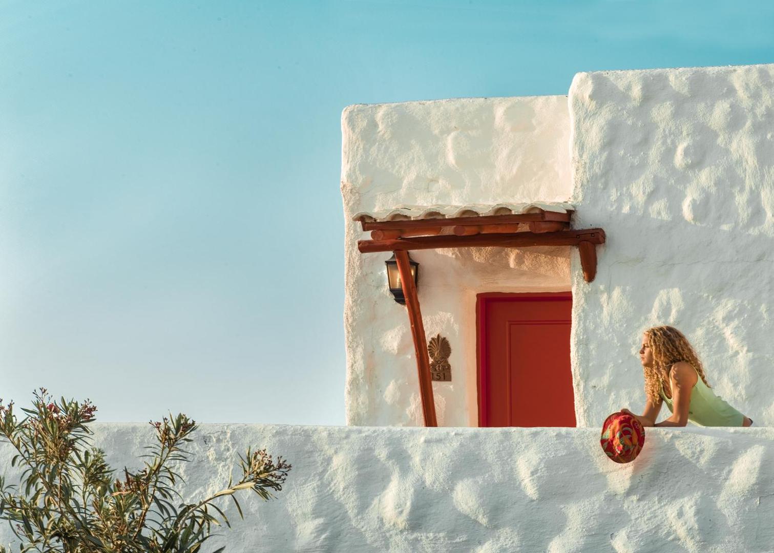 Sieviete uz Canvas by Mitsis Cretan Village numura balkona pie baltas sienas un sarkanām durvīm
