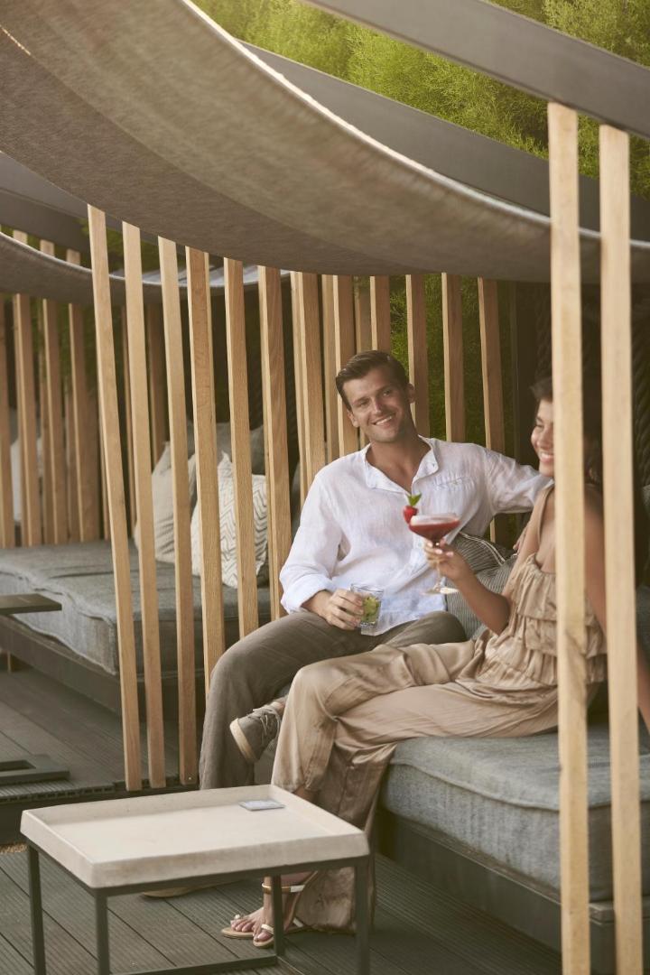 Pāris bauda kokteiļus NEMA Design Hotel & Spa atpūtas zonā zem nojumes, stilīgs dizains un vasarīga atmosfēra Krētā