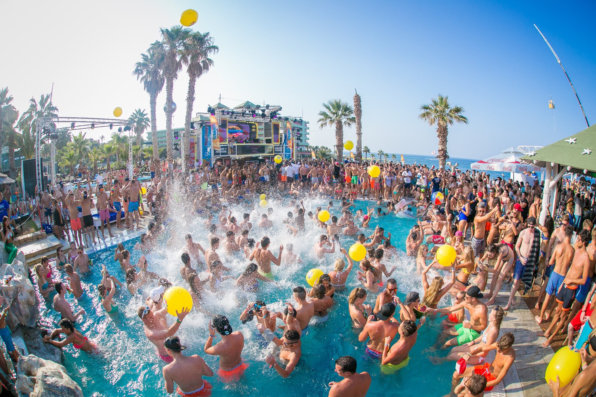 Star Beach Village & Water Park baseina ballīte ar daudziem cilvēkiem, dzeltenām bumbām un DJ skatuvi Hersonisā