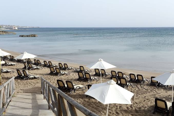 Star Beach Village & Water Park privātā smilšu pludmale ar daudziem sauļošanās krēsliem un baltiem saulessargiem pie dzidrās Egejas jūras.