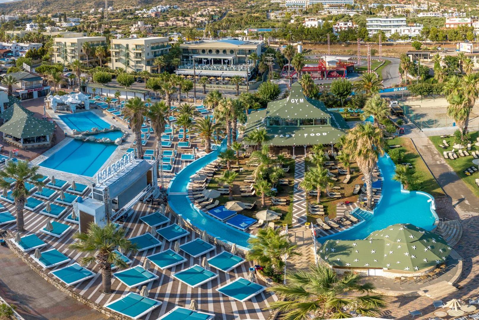 Star Beach Village & Water Park atpūtas zona ar vairākiem baseiniem, sauļošanās krēsliem, palmām un ātrās ēdināšanas restorānu Krētā