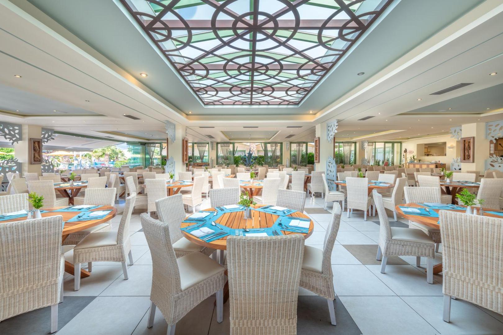 Star Beach Village & Water Park galvenais restorāns ar gaišām mēbelēm un dekoratīvu stikla griestu kupolu Hersonisā, Krētā