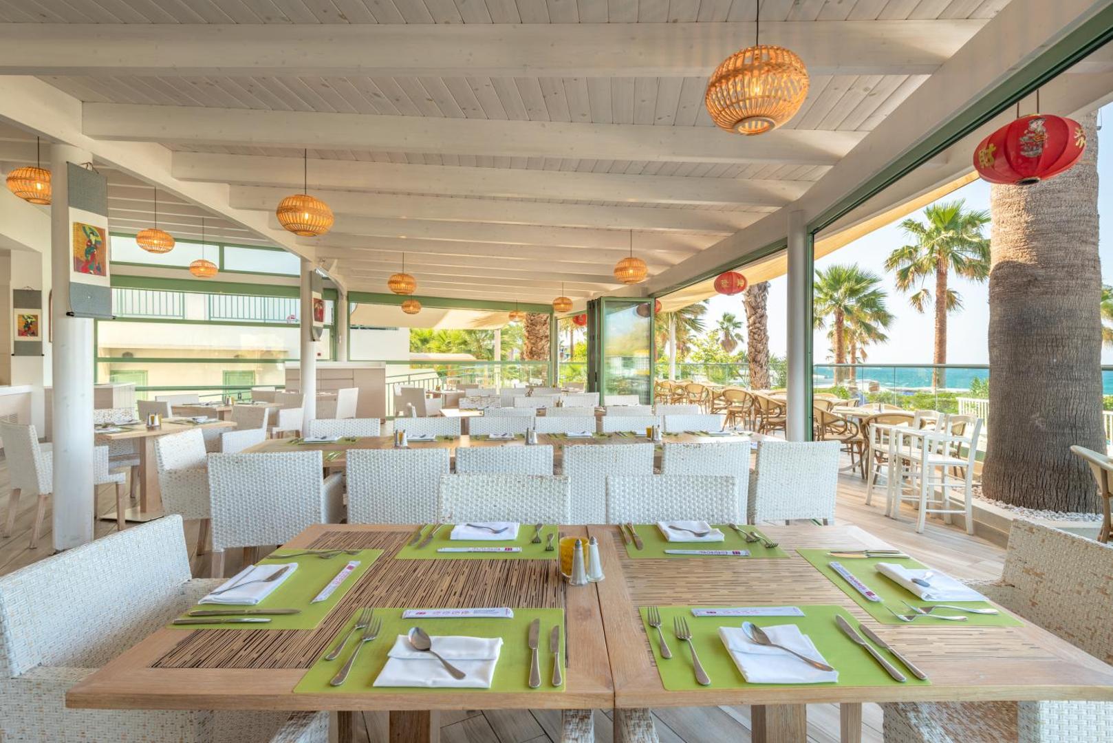 Star Beach Village & Water Park restorāna terase ar gaišām mēbelēm, bambusa dekoriem un skatu uz palmām un jūru