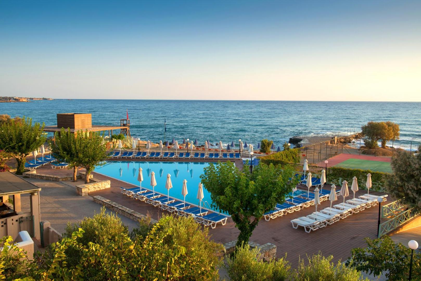 Silva Beach viesnīcas baseins tieši pie jūras krasta Hersonisā — blakus redzams tenisa korts un atpūtas zona ar zviļņiem