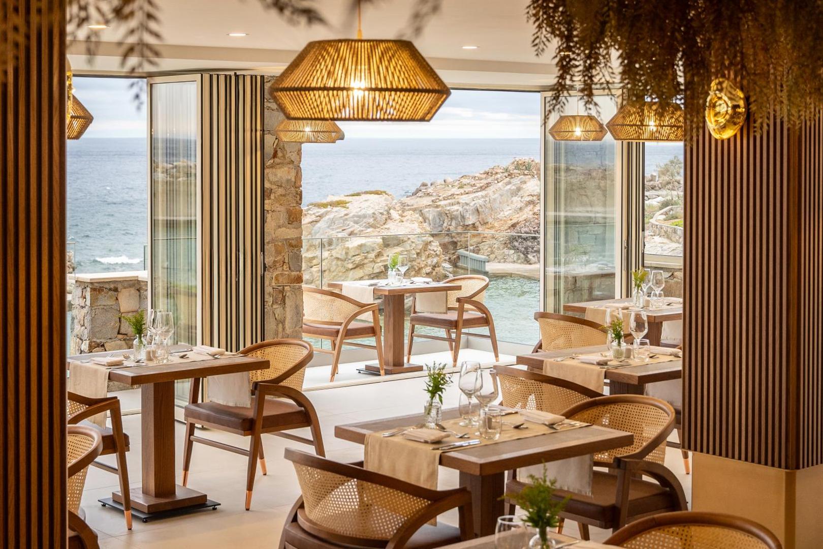 Iberostar Selection Creta Marine restorāna interjers ar panorāmas logiem uz jūru, pītiem gaismekļiem un koka mēbelēm