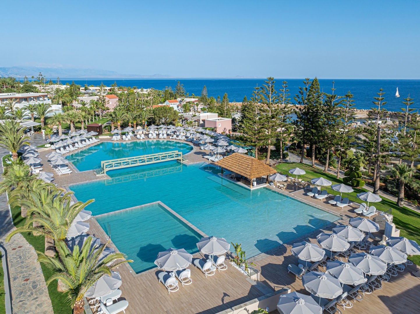 Iberostar Selection Creta Marine kūrorta panorāmas skats ar baseiniem, bāru zem niedrēm un Vidusjūras piekrasti fonā.
