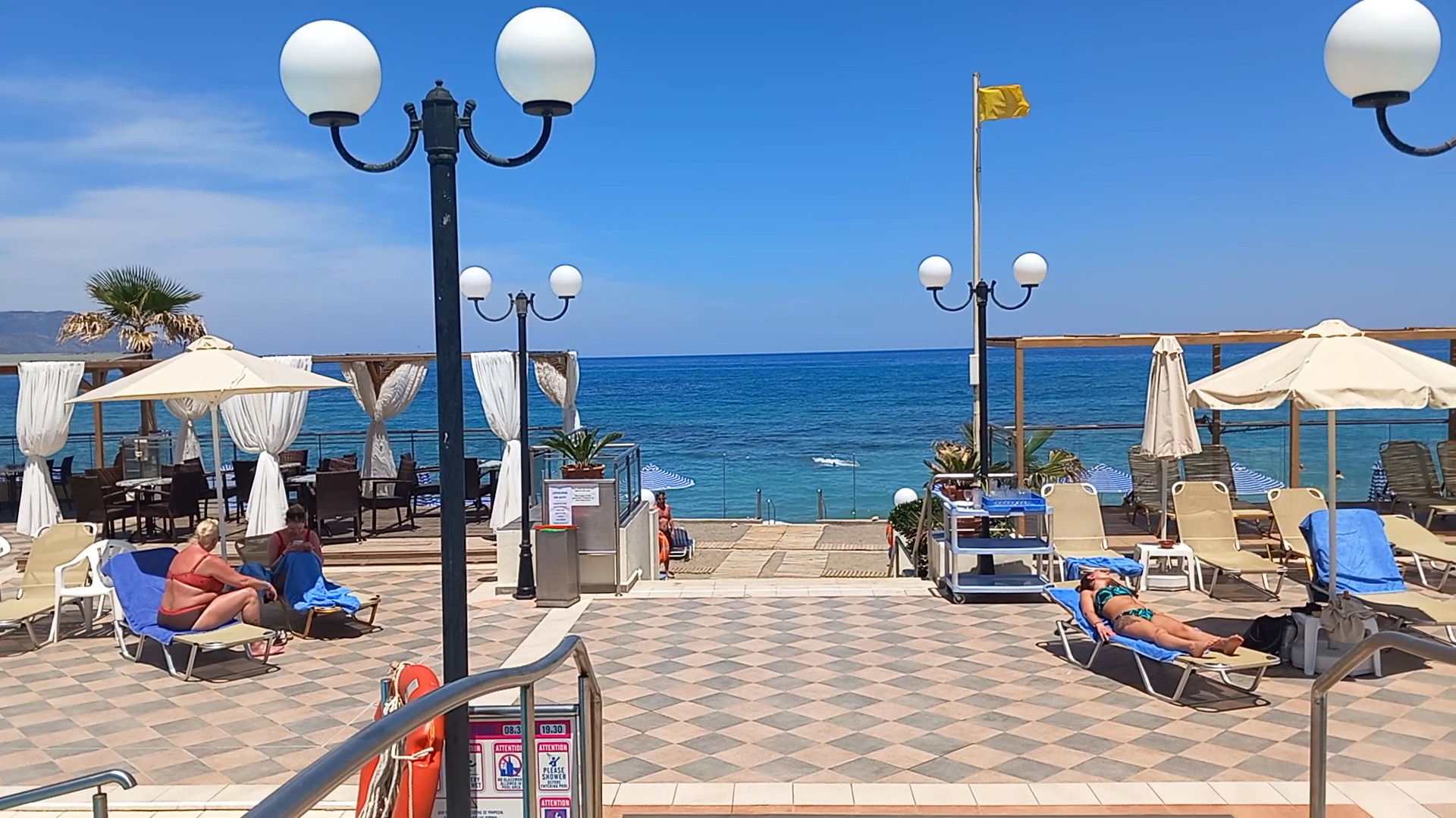 Hydramis Palace Beach Resort atpūtas zona pie jūras ar flīzētu terasi, saulessargiem, zviļņiem un dekoratīvām ielu laternām