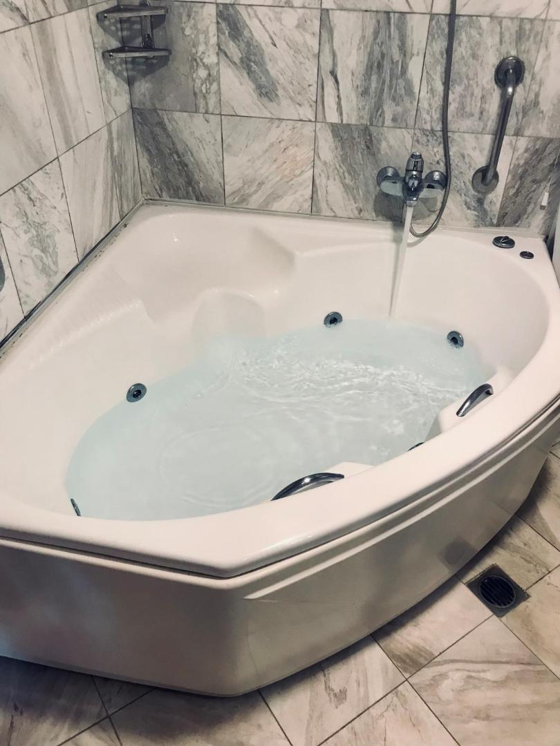 Tuvplāns stūra džakuzi vannai ar tekošu ūdeni Hydramis Palace Beach Resort numurā, flīzētas sienas un grīda
