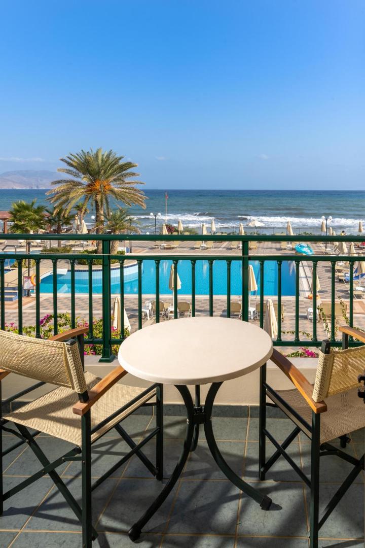 Hydramis Palace Beach Resort numura balkons ar skatu uz āra baseinu un Vidusjūru Krētā — mēbelēta terase atpūtai piekrastē