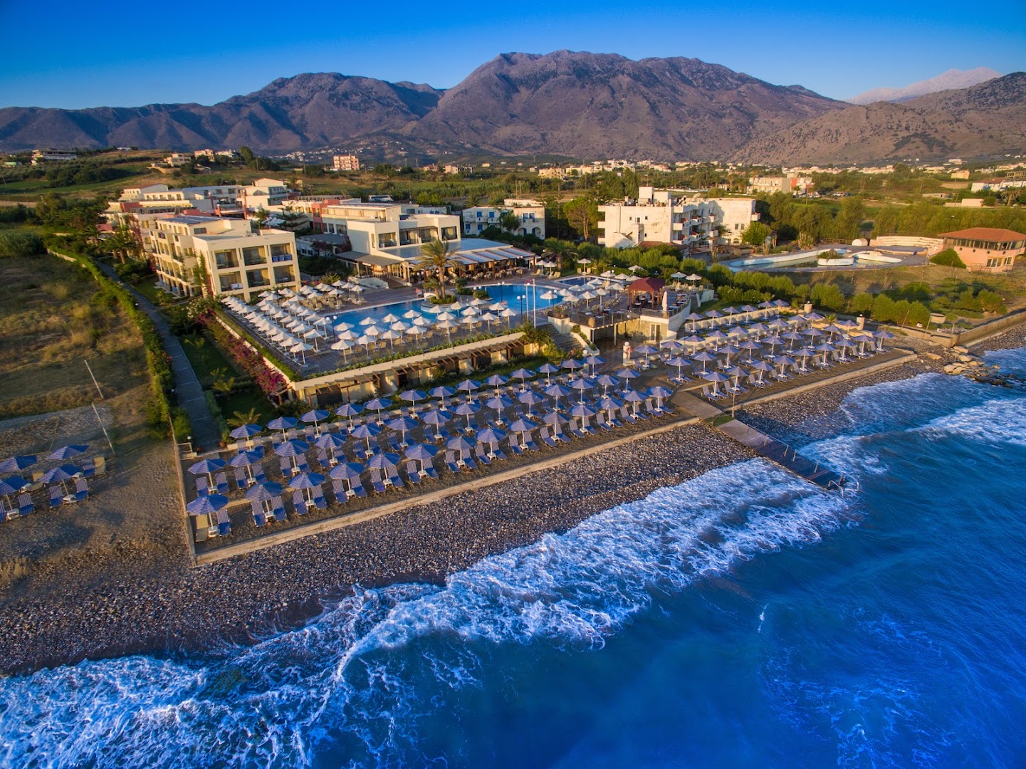 Hydramis Palace Beach Resort panorāmas skats ar pludmali, saulessargiem, baseinu un iespaidīgiem kalniem fonā Georgiupoles reģionā