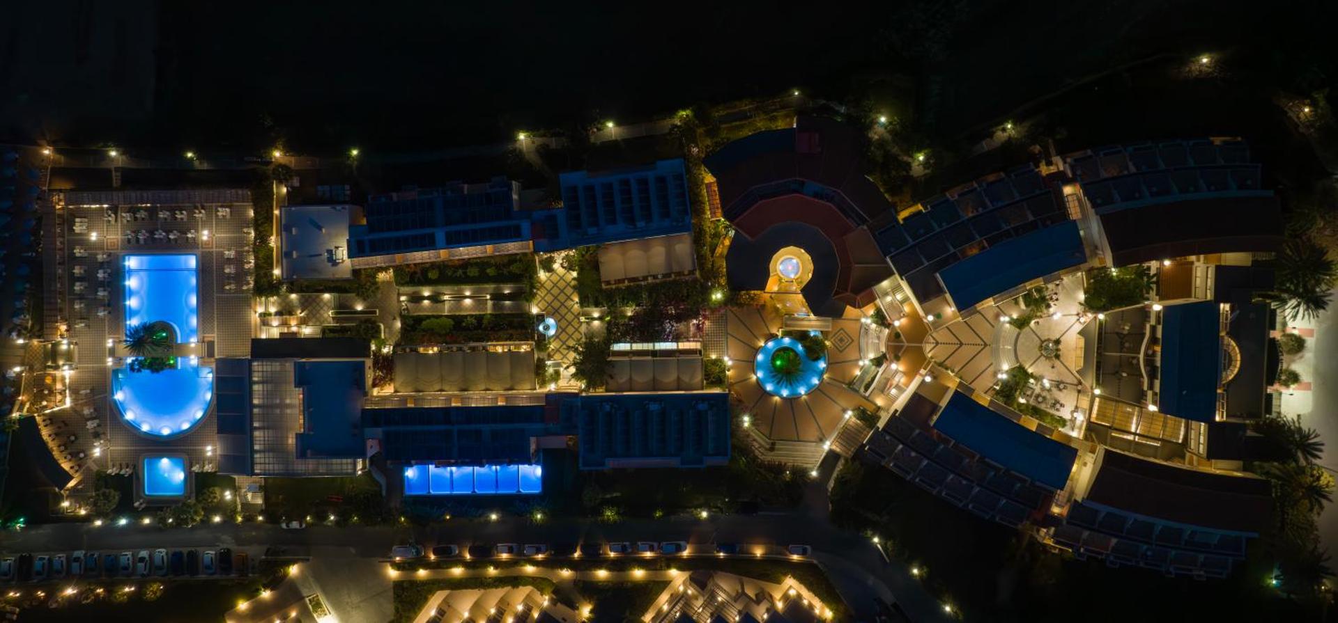 Hydramis Palace Beach Resort teritorijas nakts skats no putna lidojuma ar izgaismotiem baseiniem un viesnīcas korpusiem Krētā