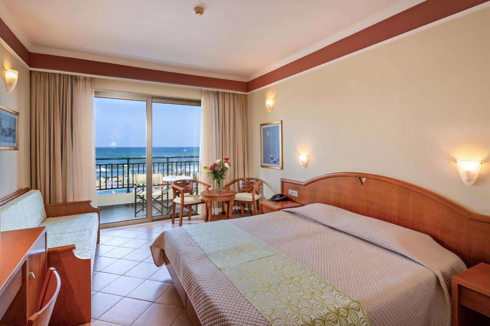 Hydramis Palace Beach Resort gaišs viesnīcas numurs ar divguļamo gultu, dīvānu un balkonu ar skatu uz jūru Krētas piekrastē