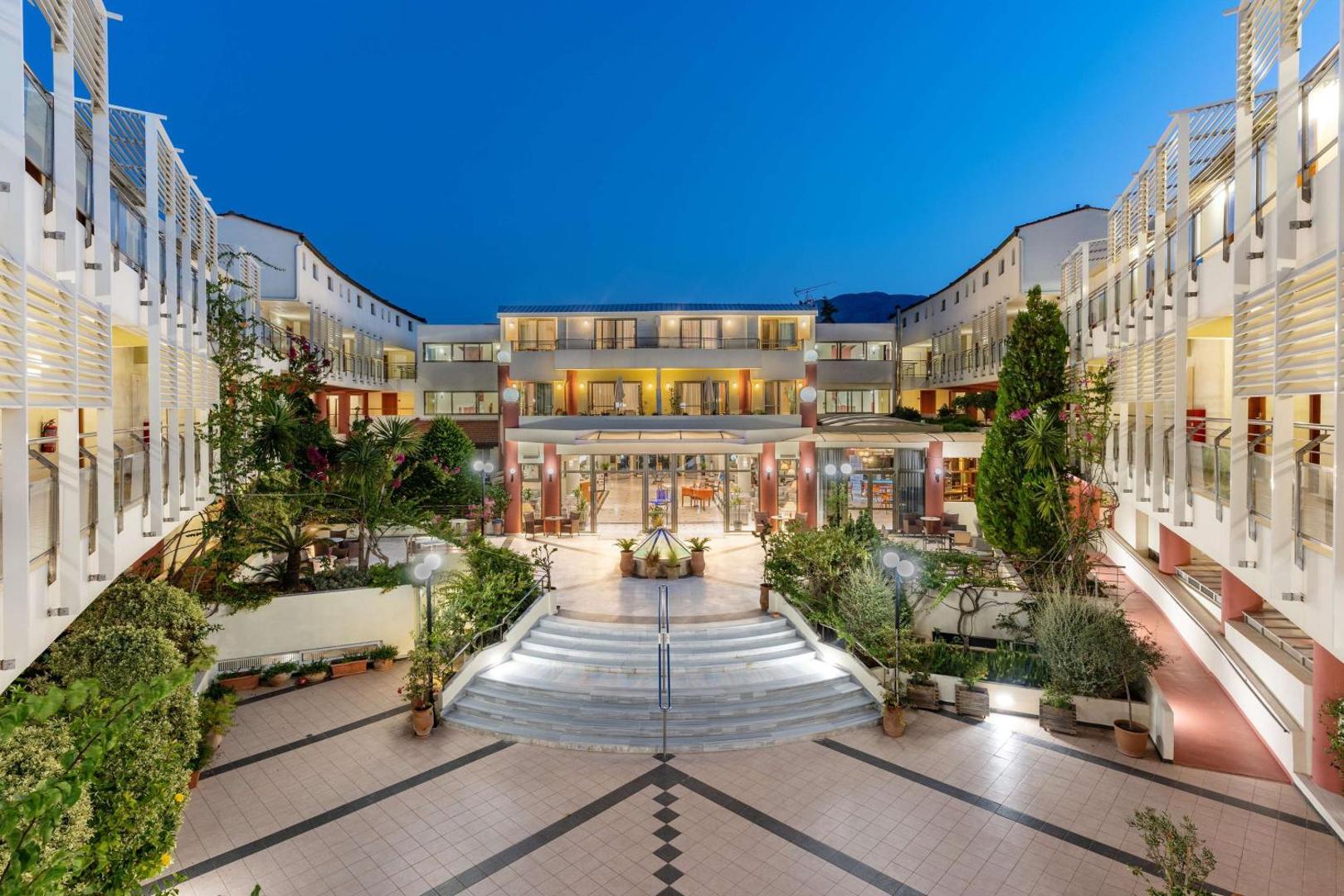 Hydramis Palace Beach Resort viesnīcas iekšpagalms un ieeja vakara apgaismojumā ar modernu arhitektūru un koptiem augiem