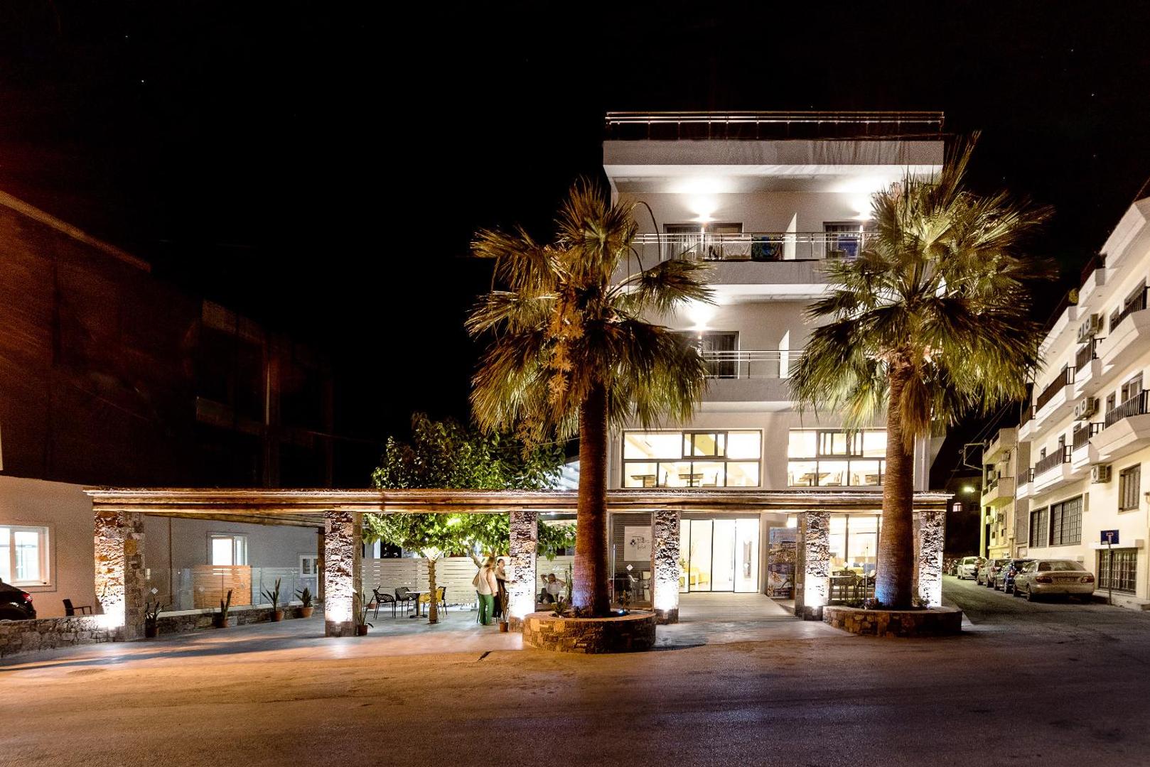 Pollis Hotel ieeja un terase nakts apgaismojumā — izgaismotas palmas un mājīga atpūtas zona pie viesnīcas galvenās ēkas