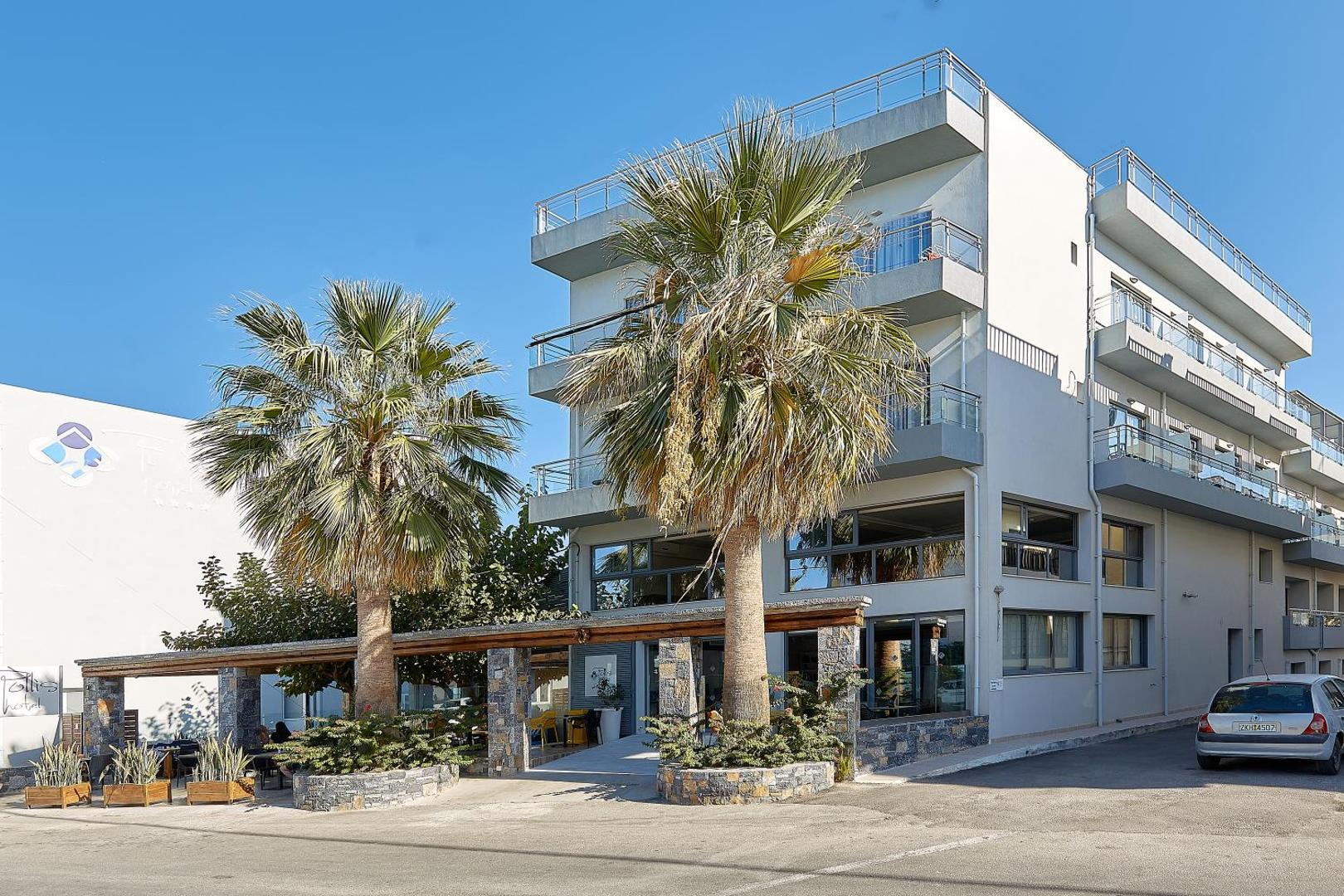 Pollis Hotel modernā fasāde Hersonisā, Krētā — četru stāvu ēka ar balkoniem, palmām un āra terasi saulainā dienā