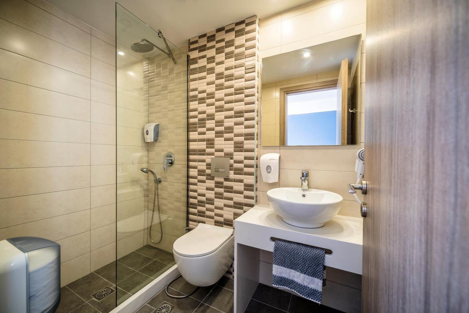 Pollis Hotel numura vannasistaba ar stikla dušas kabīni, modernu izlietni un gaišām flīzēm — mūsdienīgs dizains un tīrība