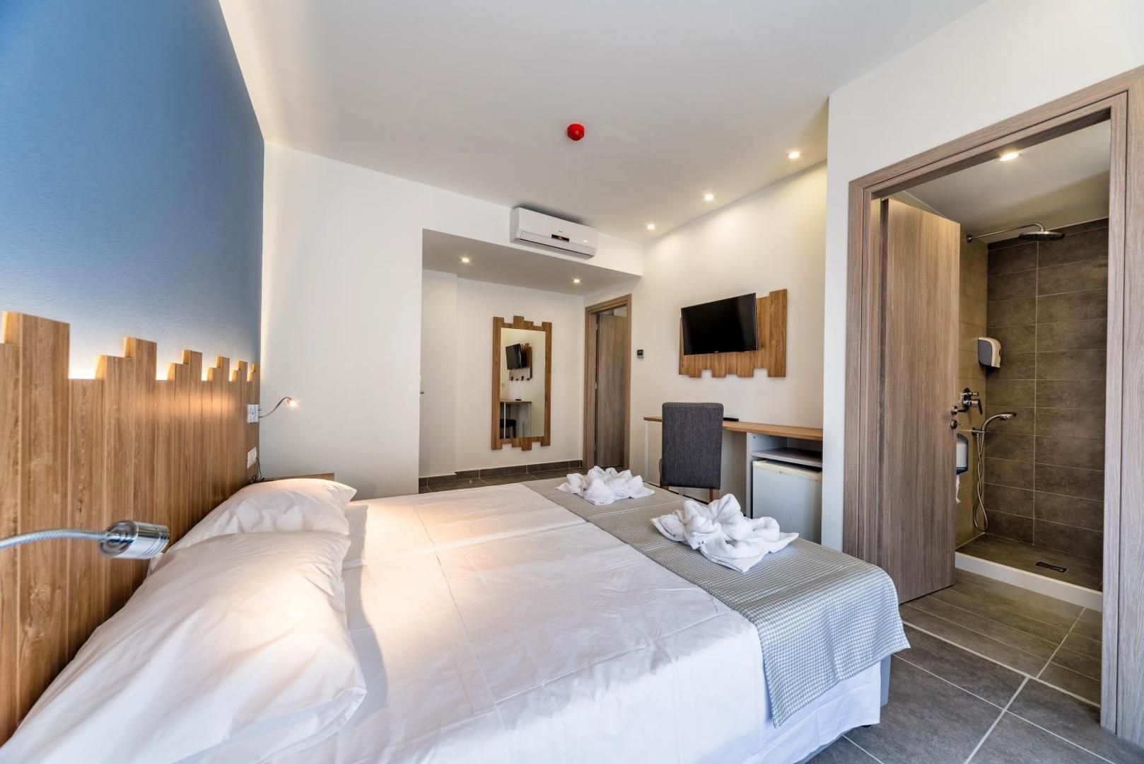 Pollis Hotel numura skats uz vannasistabu ar dušu — redzama gulta, gaisa kondicionieris un spogulis pie sienas