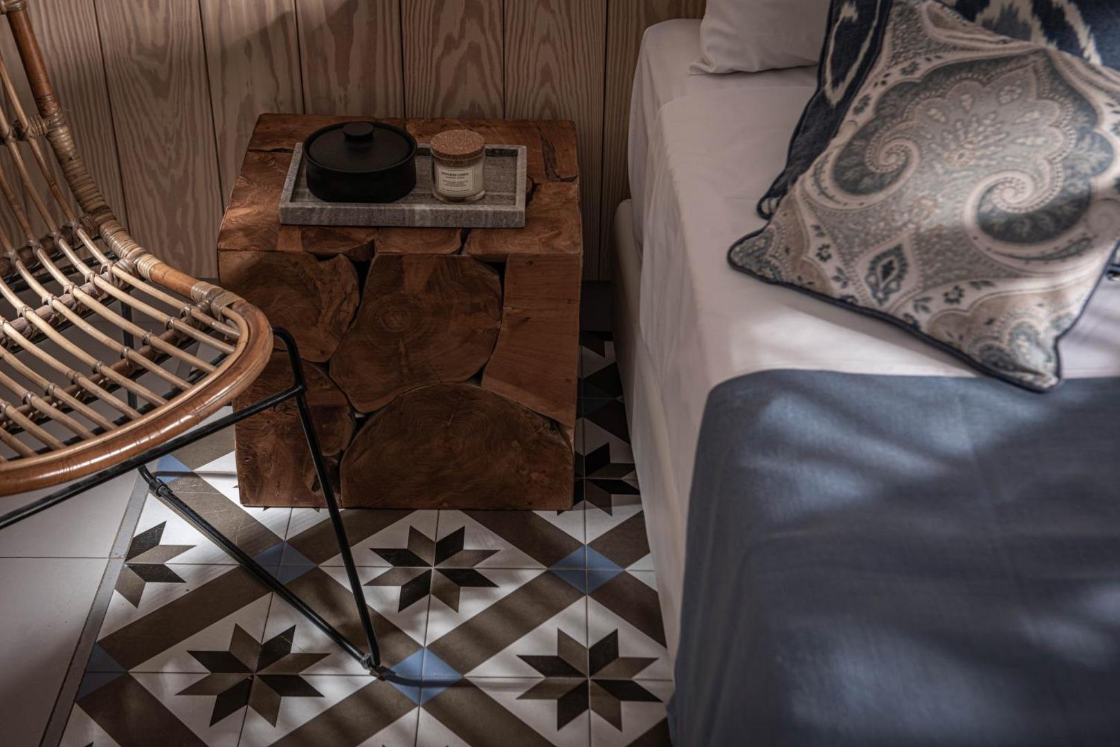 Serenity Spritz Boutique Hotel interjera detaļa ar masīvkoka naktsskapīti, pītu krēslu un rakstainām grīdas flīzēm numurā.