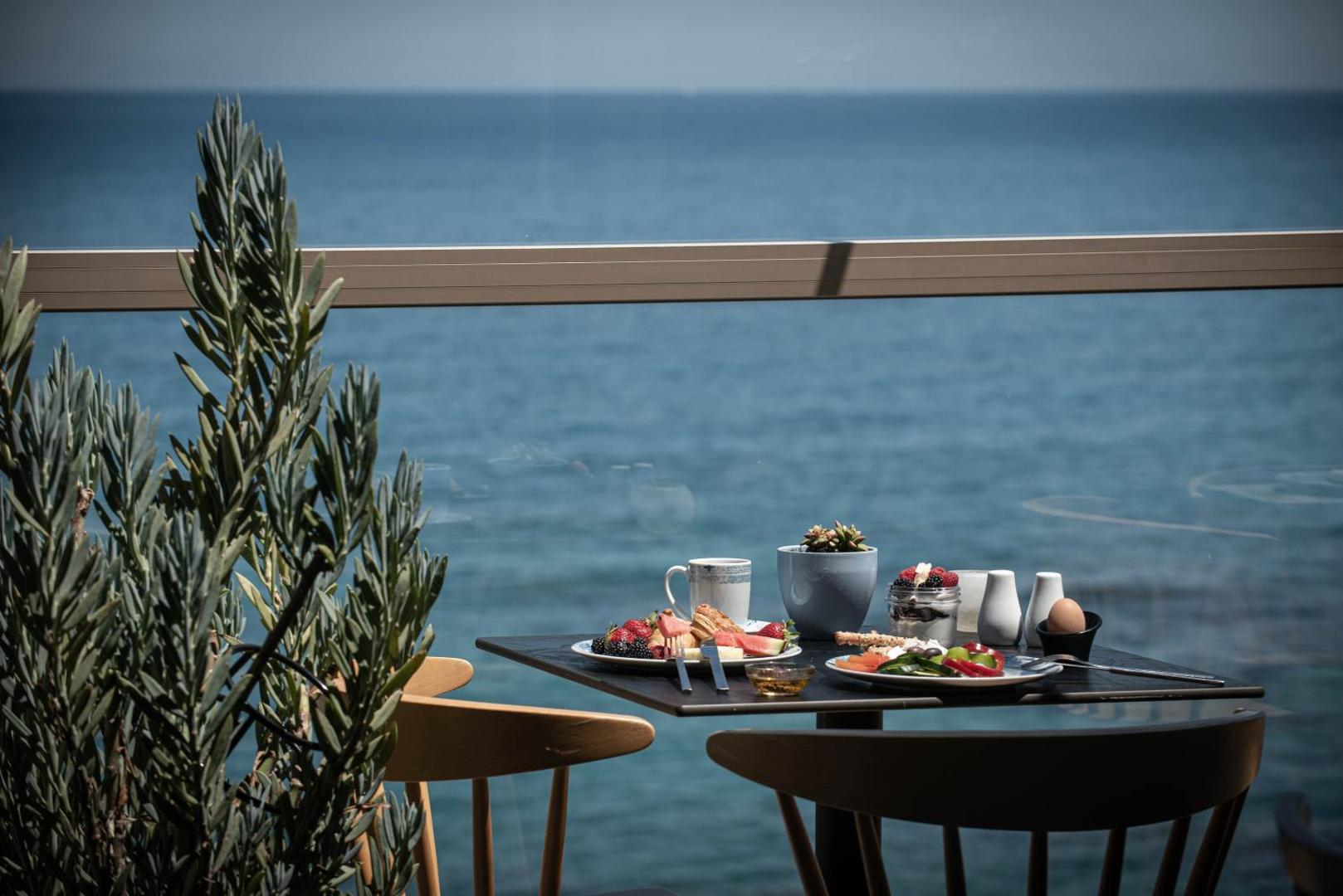 Brokastis uz Serenity Spritz Boutique Hotel terases ar skatu uz jūru — galds ar augļiem un kafiju pie stikla margām
