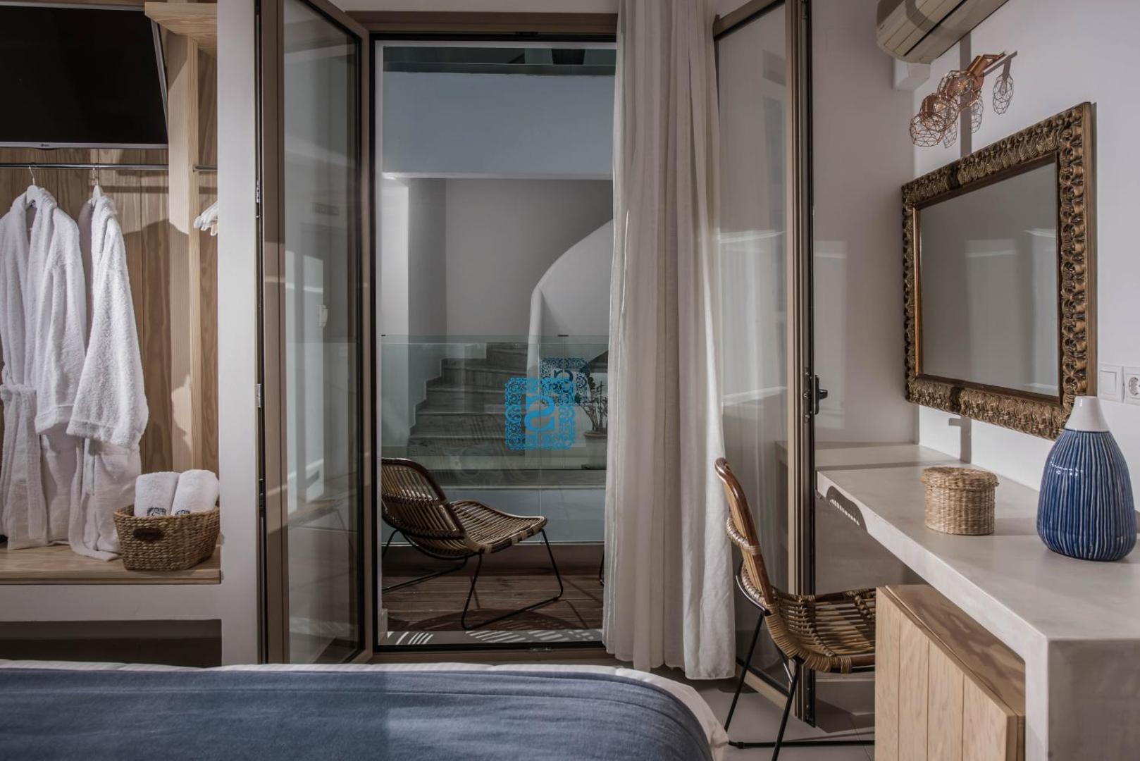 Serenity Spritz Boutique Hotel numura skats uz terasi ar pītu krēslu, darba galdu un spoguli zeltītā rāmī.