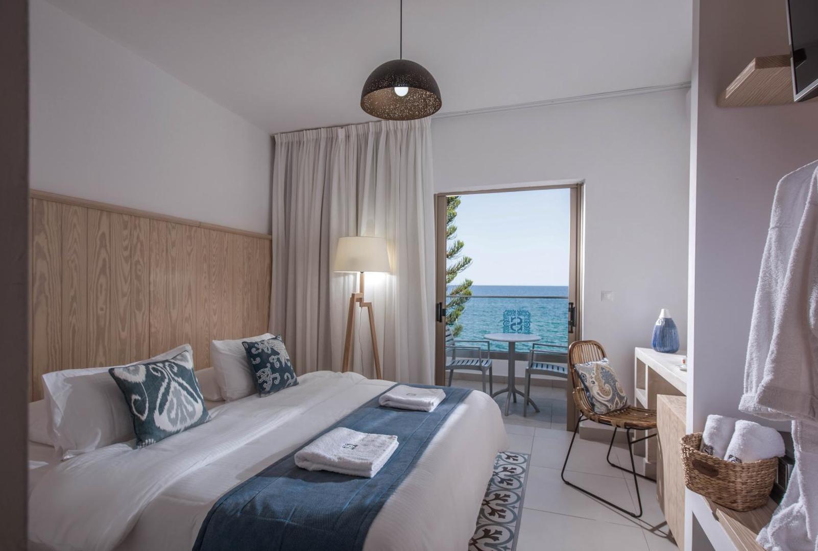 Serenity Spritz Boutique Hotel gaišs numurs ar skatu uz jūru, balkonu, divguļamo gultu un koka apdares elementiem piekrastē.