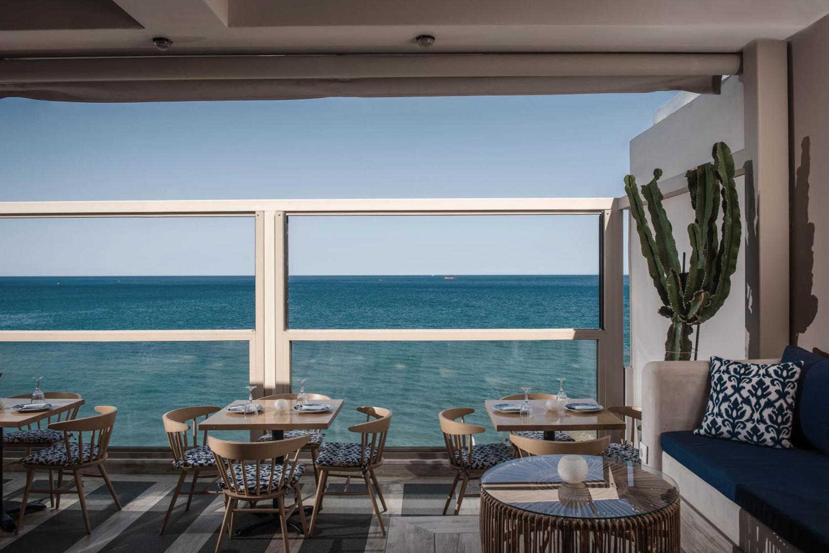 Serenity Spritz Boutique Hotel restorāna terase ar skatu uz jūru, elegantiem koka galdiem un ziliem akcentiem interjerā