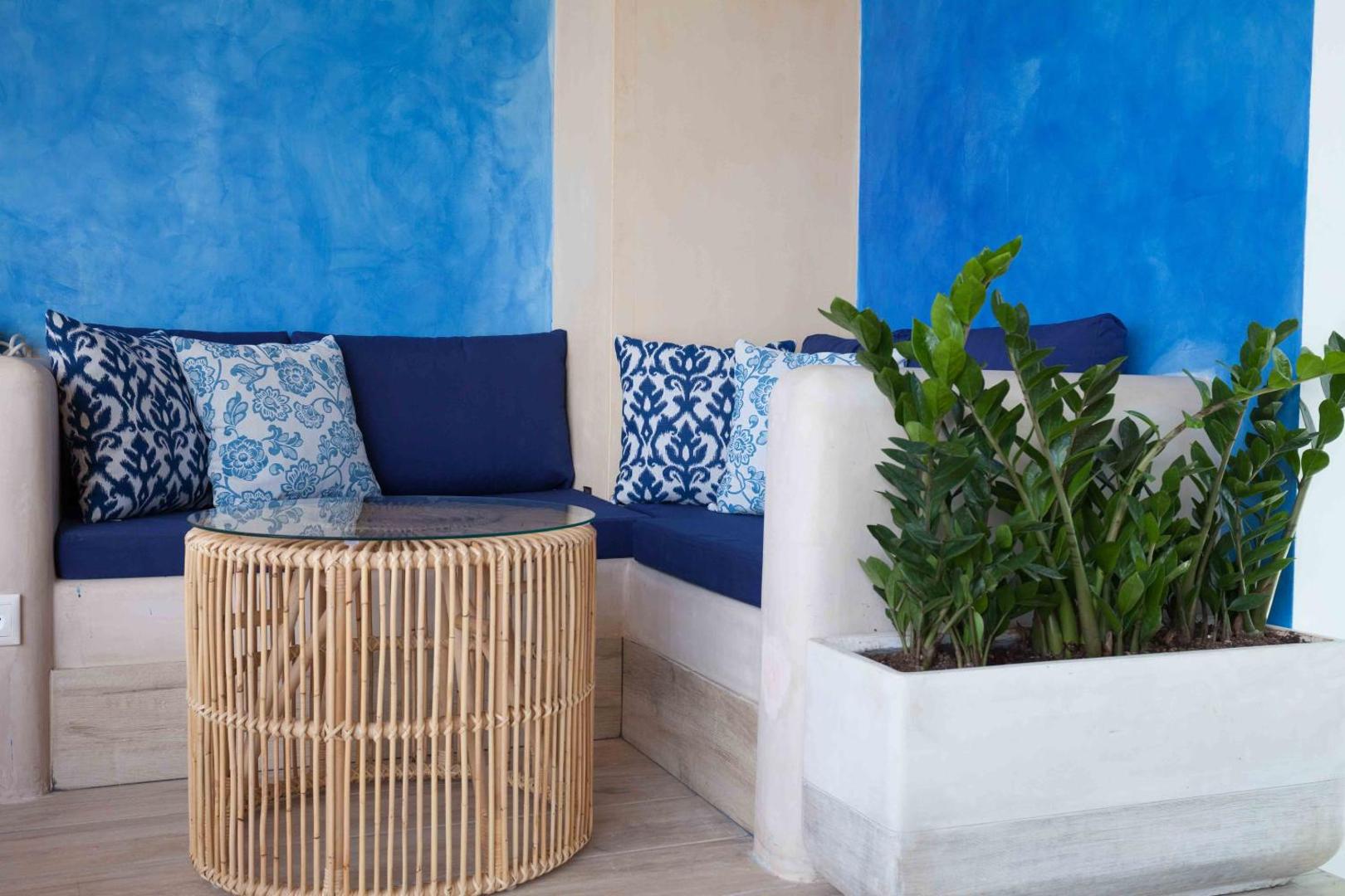 Serenity Spritz Boutique Hotel atpūtas zona ar ziliem dīvāniem, rakstainiem spilveniem un pītu galdiņu Grieķijas salu stilā piekrastē