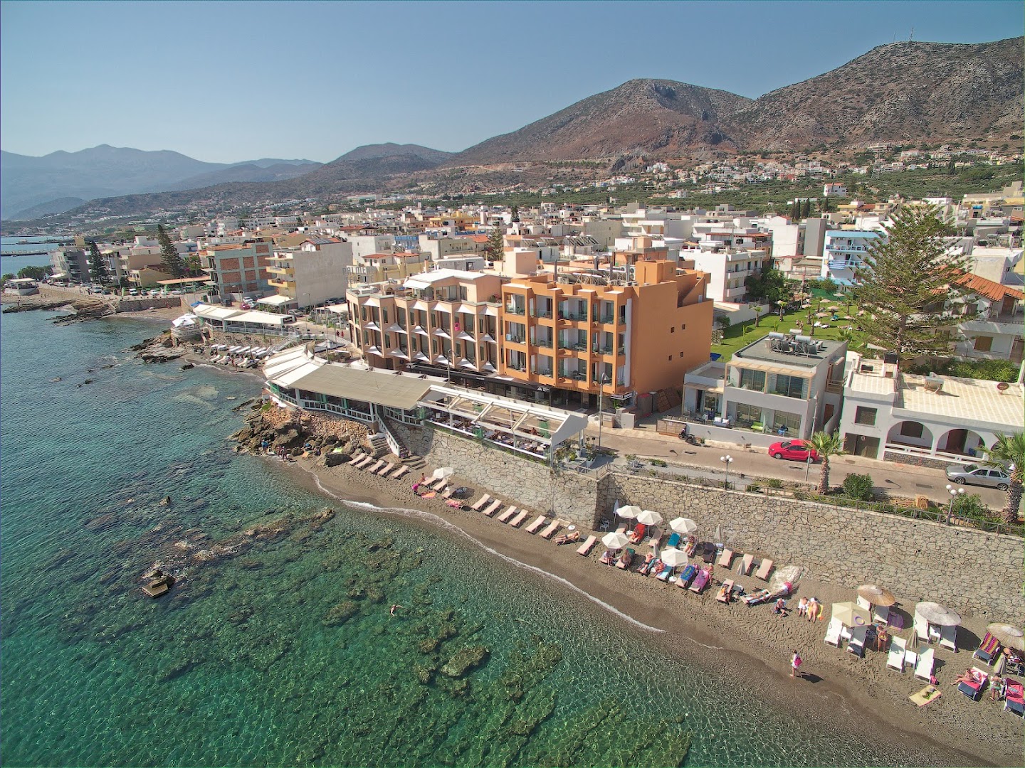 Palmera Beach Hotel & Spa panorāmas skats dienā Hersonisā — viesnīcas ēka, pludmales zona un kalni fonā zem skaidrām debesīm