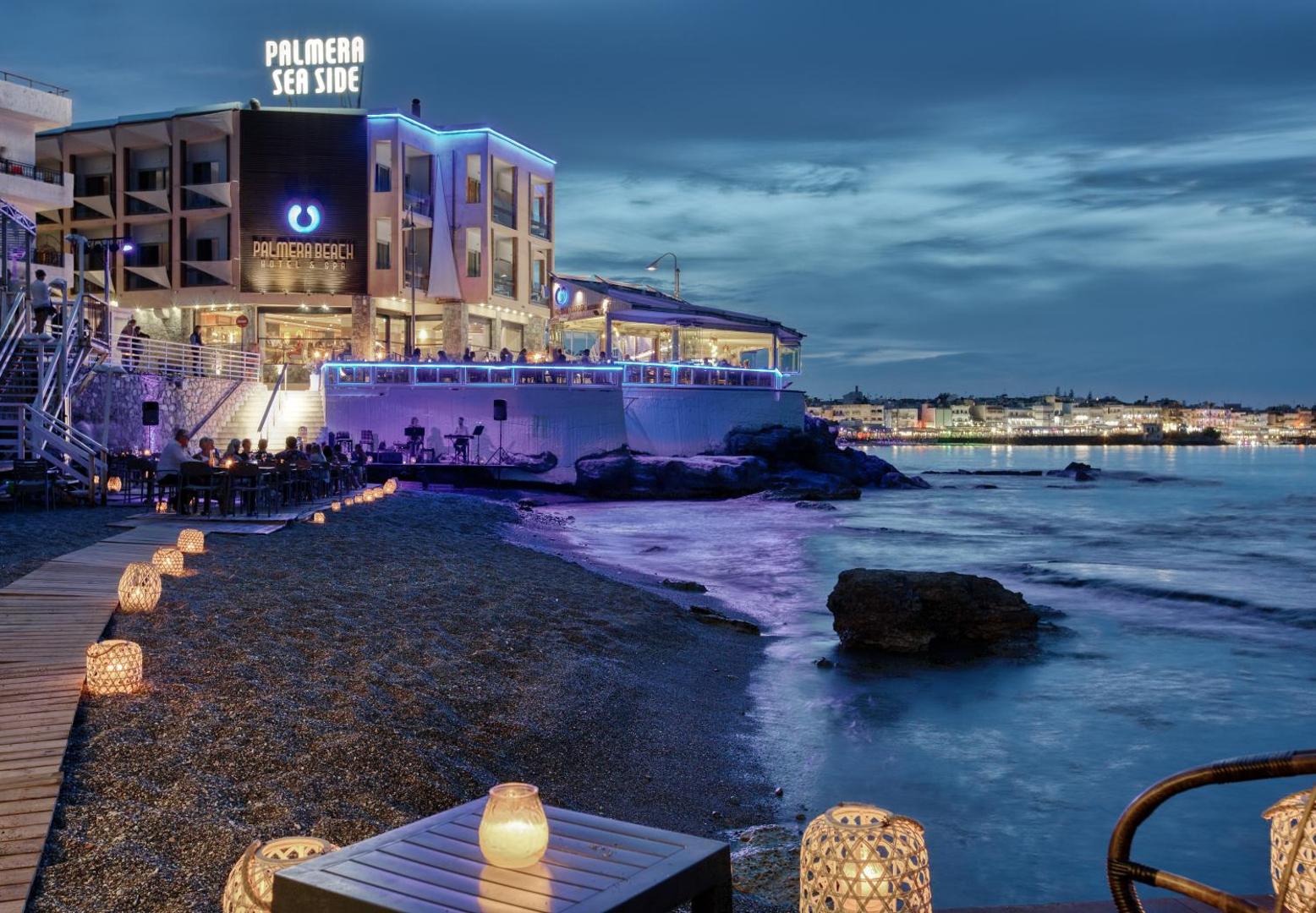 Palmera Beach Hotel & Spa pludmales zona krēslas stundā ar dekoratīvām laternām un skatu uz Hersonisas līci Krētā