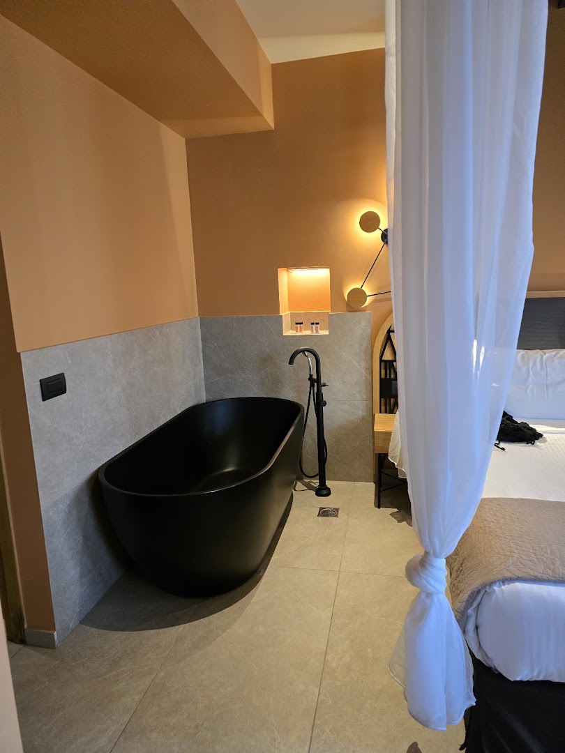 Moderns Palmera Beach Hotel & Spa viesnīcas numurs ar melnu dizaina vannu blakus gultai un siltu apgaismojumu mājīgai atmosfērai.