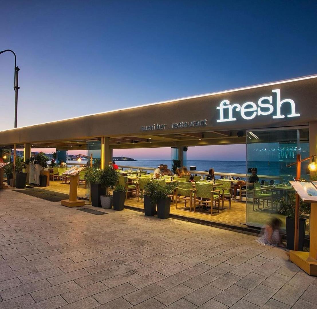 Viesnīcas Palmera Beach Hotel & Spa restorāns Fresh saulrieta laikā — moderna āra terase ar skatu uz jūru