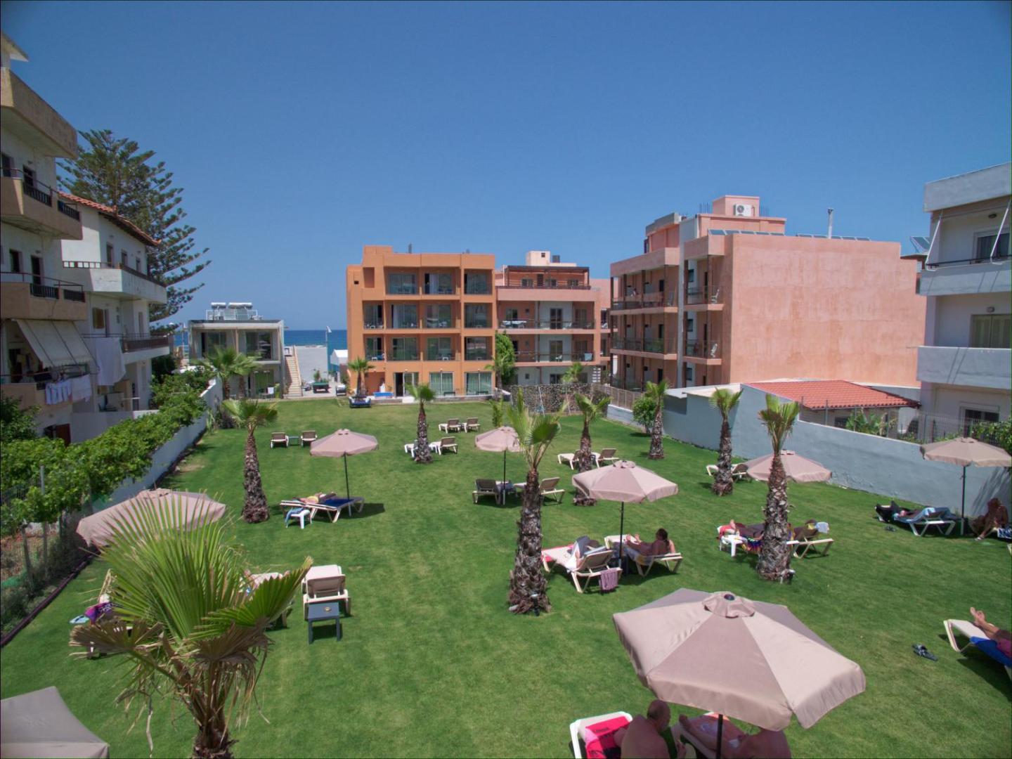 Palmera Beach Hotel & Spa zālājs ar sauļošanās krēsliem un saulessargiem — atpūtas zona starp palmām viesnīcas iekšpagalmā