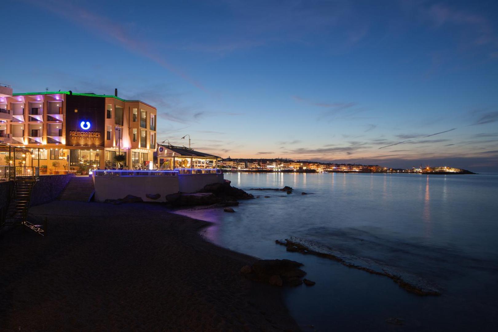 Palmera Beach Hotel & Spa skats vakarā no pludmales — izgaismota viesnīcas ēka un restorāns pie jūras Hersonisā